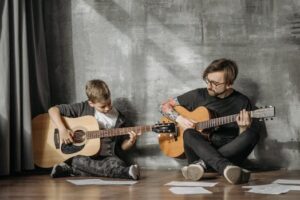 A heartwarming scene of a man teaching a boy to play guitar indoors.